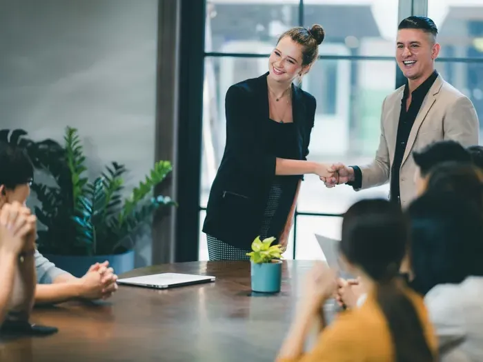 Team applauds as two professionals shake hands in a meeting room, symbolizing partners on City Directory Spot